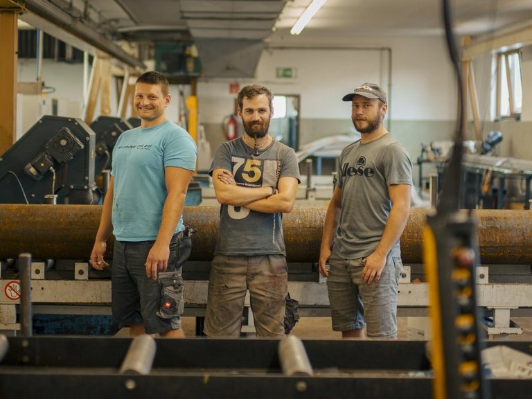 drei Maenner stehen in der Werkstatt und lachen in die Kamera
